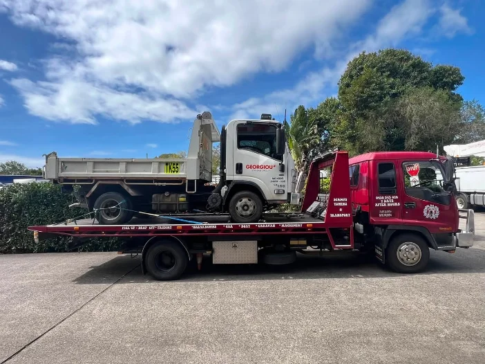 Large tip truck loaded on red tow truck on suburban street