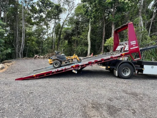Ride-on mower loading up ramp of red tow truck in rainforest