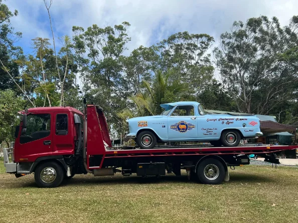 Classic light blue car on red tow truck in FNQ
