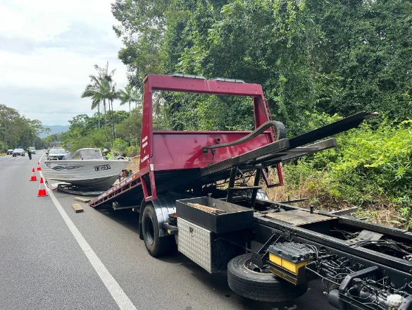 Boat being loaded onto red tow truck on a coastal road, Port Douglas area