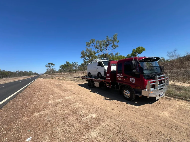 Van on red tow truck on a dry outback road through the Tablelands