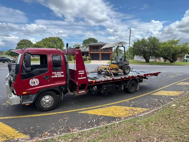 Ride-on mower on red tow truck on suburban street